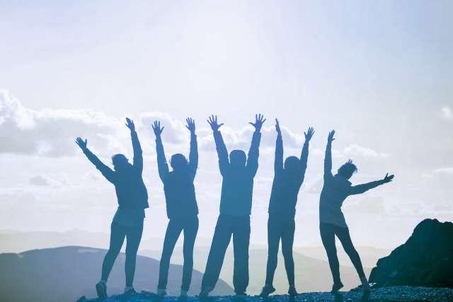 Group of people standing on mountain top with hands up in the air